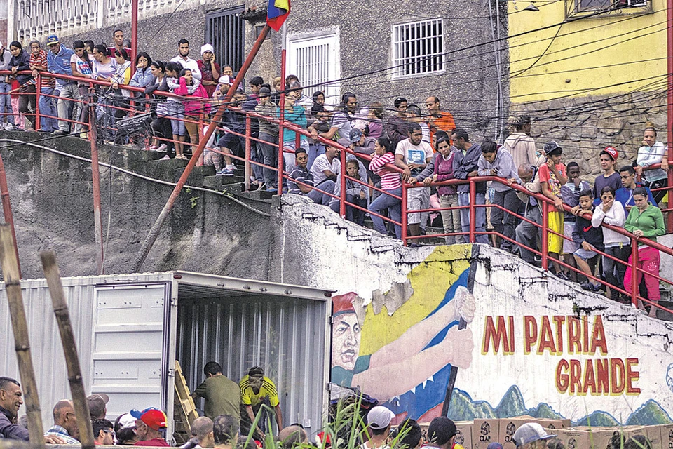 На фоне граффити с изображением экс-президента Уго Чавеса жители Каракаса стоят в очереди за едой, распределяемой правительством.