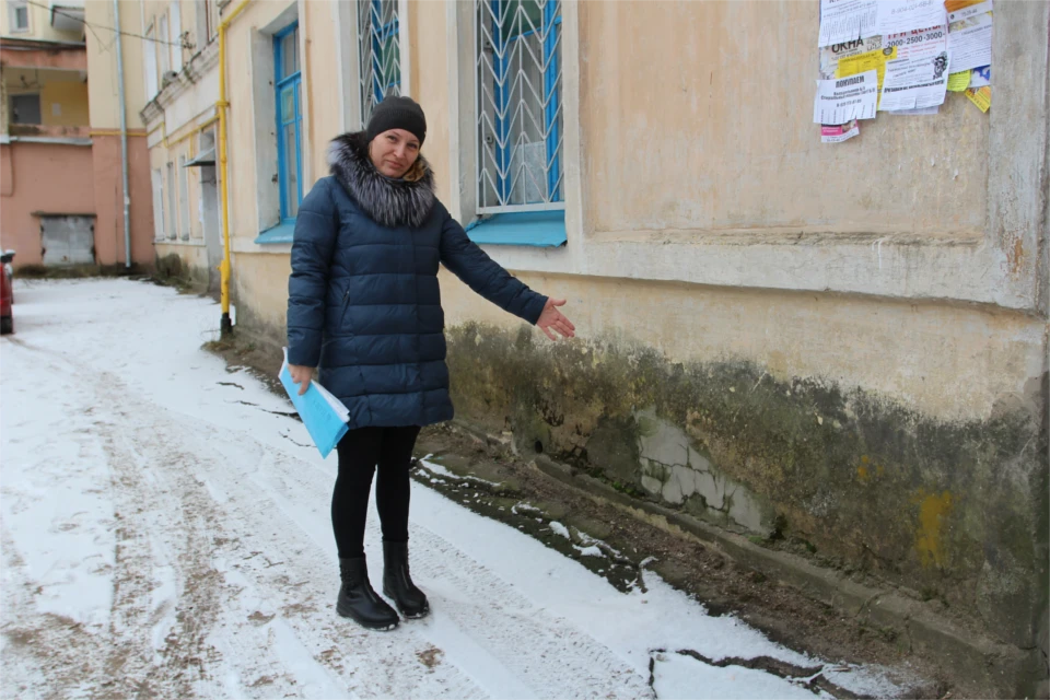 Старшая по дому Ольга Васина демонстрирует, что сделала вода со стенами дома.