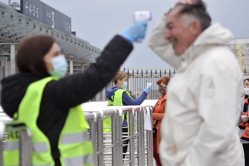 Волонтер измеряет температуру тела у болельщиков на входе на футбольный стадион 'Екатеринбург-арена' перед началом матча премьер-лиги 'Урал' - 'Рубин'.