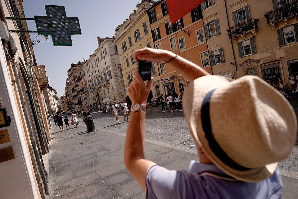 Туристка фотографирует табло с уличной температурой в Риме.