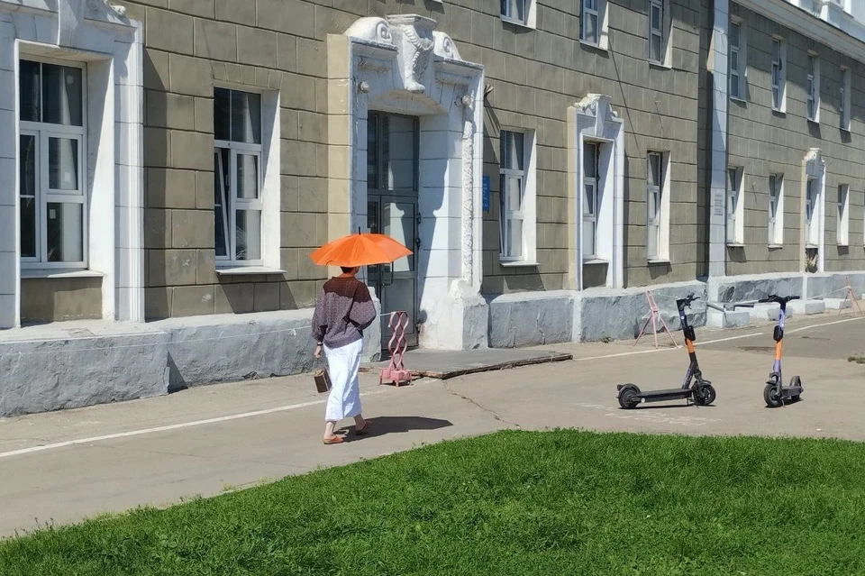 Женщина прячется от жары под зонтом.