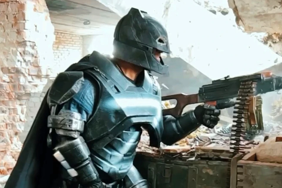 Боец в костюме Бэтмена лупит по противнику из пулемета.
