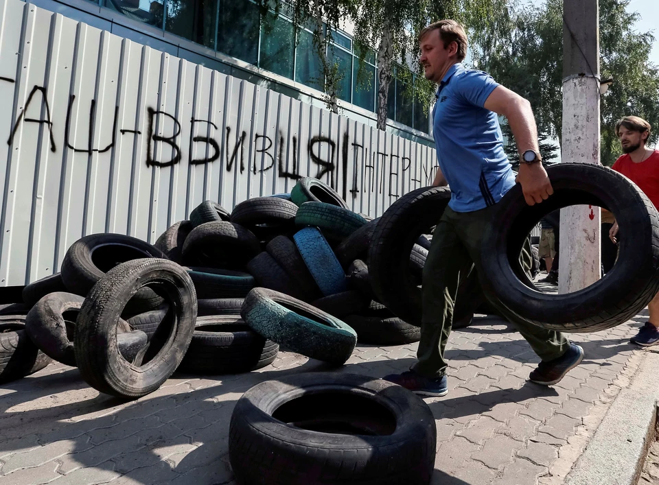 Активист подносит шины к забору, окружающему здание телеканала Интер.